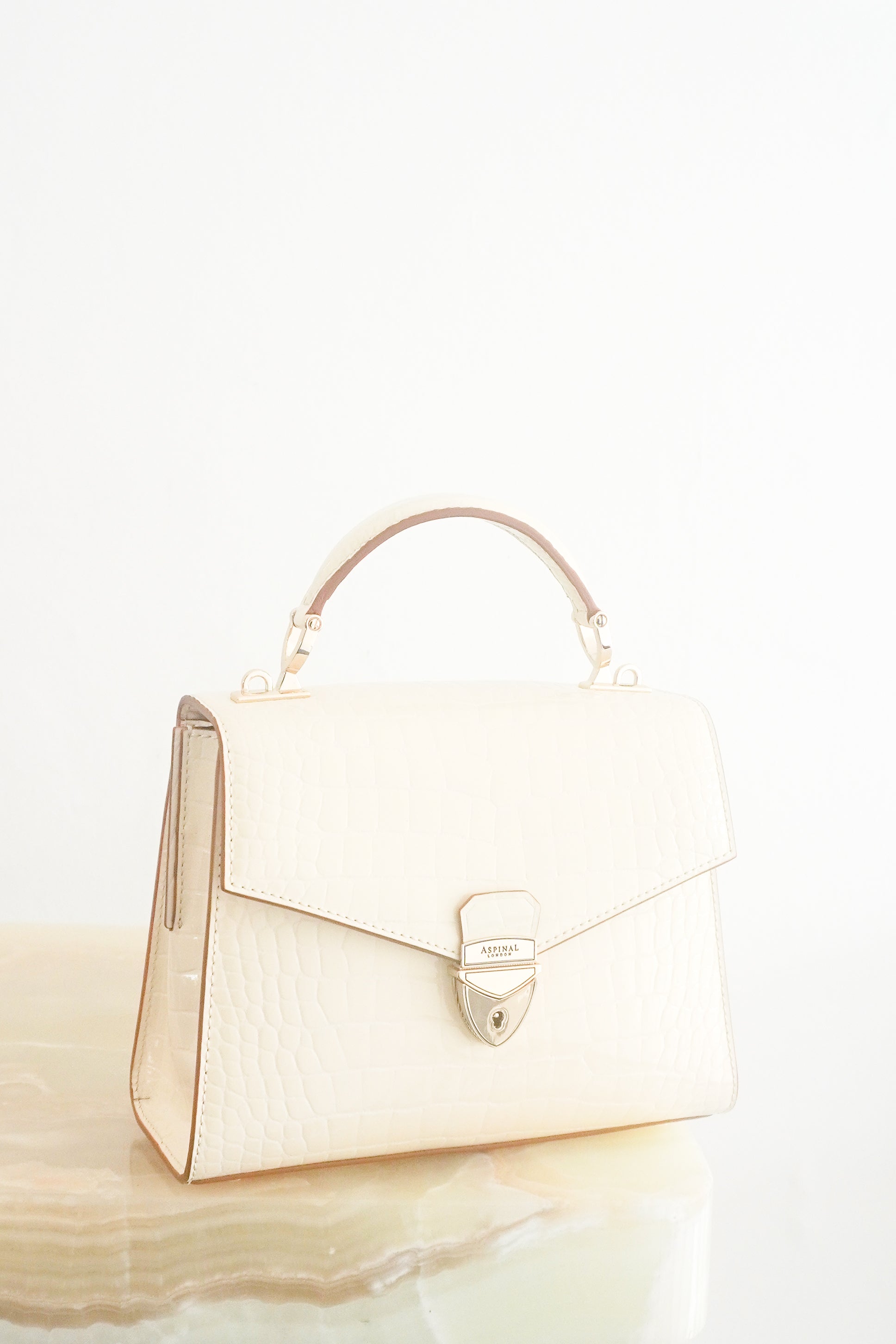 Front photo of Aspinal of London Mayfair crossbody bag in white croc-effect leather with a top handle and signature shield lock hardware.