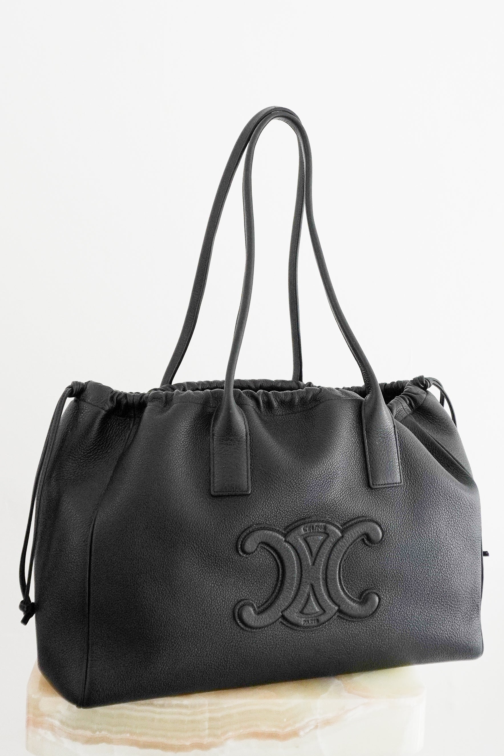 Front photo Celine Cuir Triomphe Cabas Drawstring Tote, crafted from luxurious black grained calfskin leather and featuring the house's iconic oversized embossed Triomphe logo to the front.