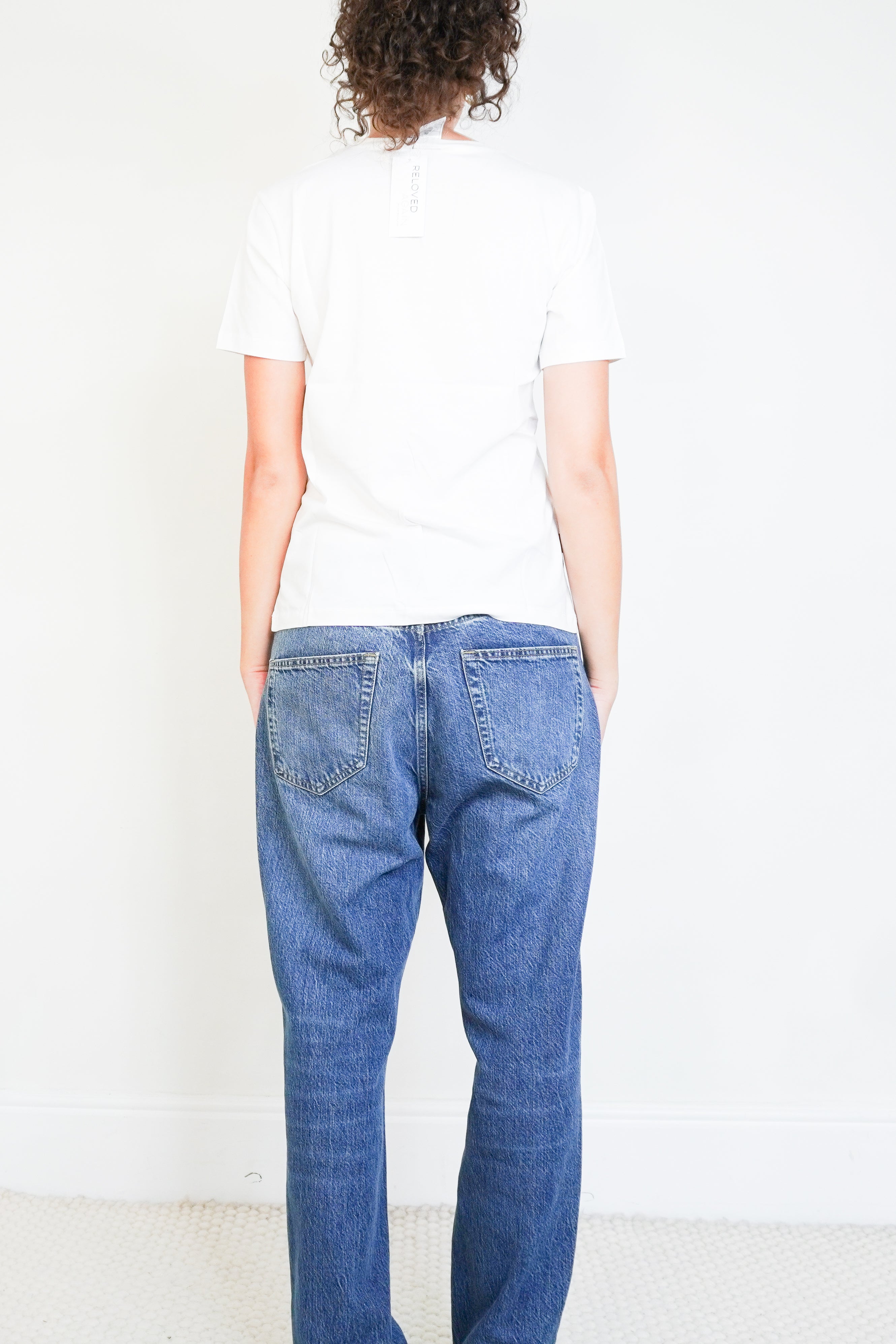 back photo of a Chanel white short-sleeved T-shirt featuring a subtle CC crystal logo detail on the side hem, paired with blue jeans.