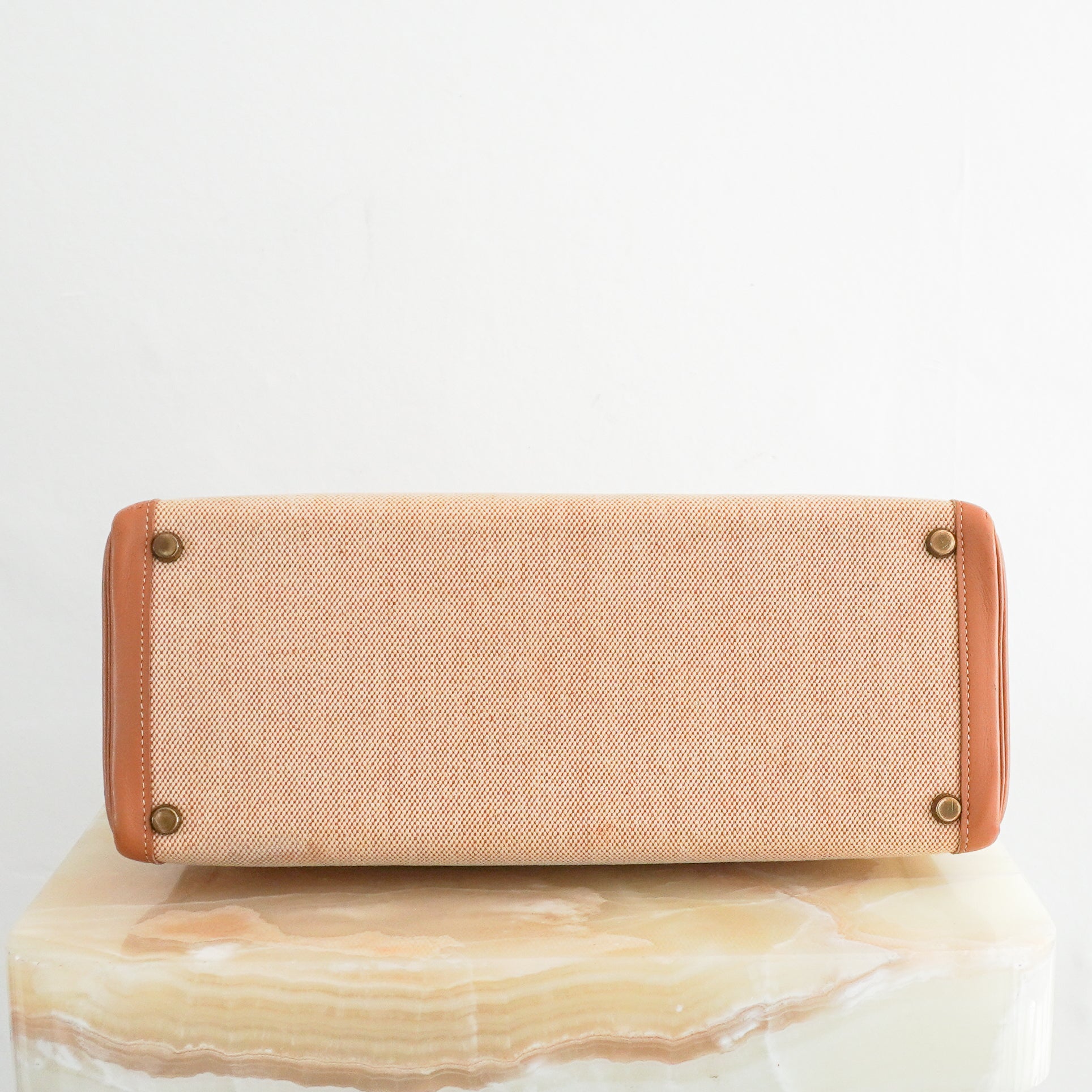 Bottom photo of an Hermès Kelly 32 handbag featuring tan Courchevel leather trim, a natural beige toile canvas body, gold-tone hardware, and a coordinating chevron patterned shoulder strap.