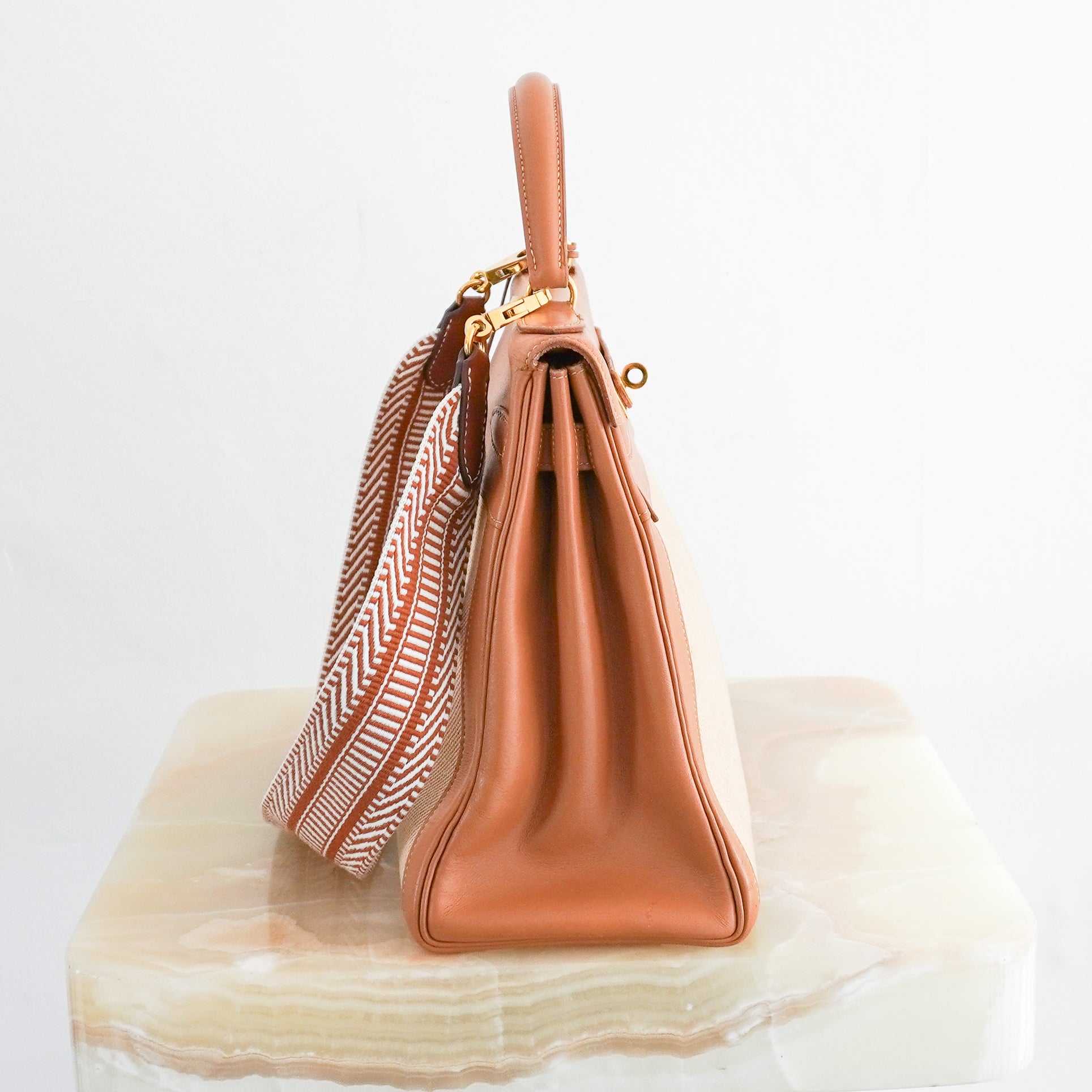 Side photo of an Hermès Kelly 32 handbag featuring tan Courchevel leather trim, a natural beige toile canvas body, gold-tone hardware, and a coordinating chevron patterned shoulder strap.