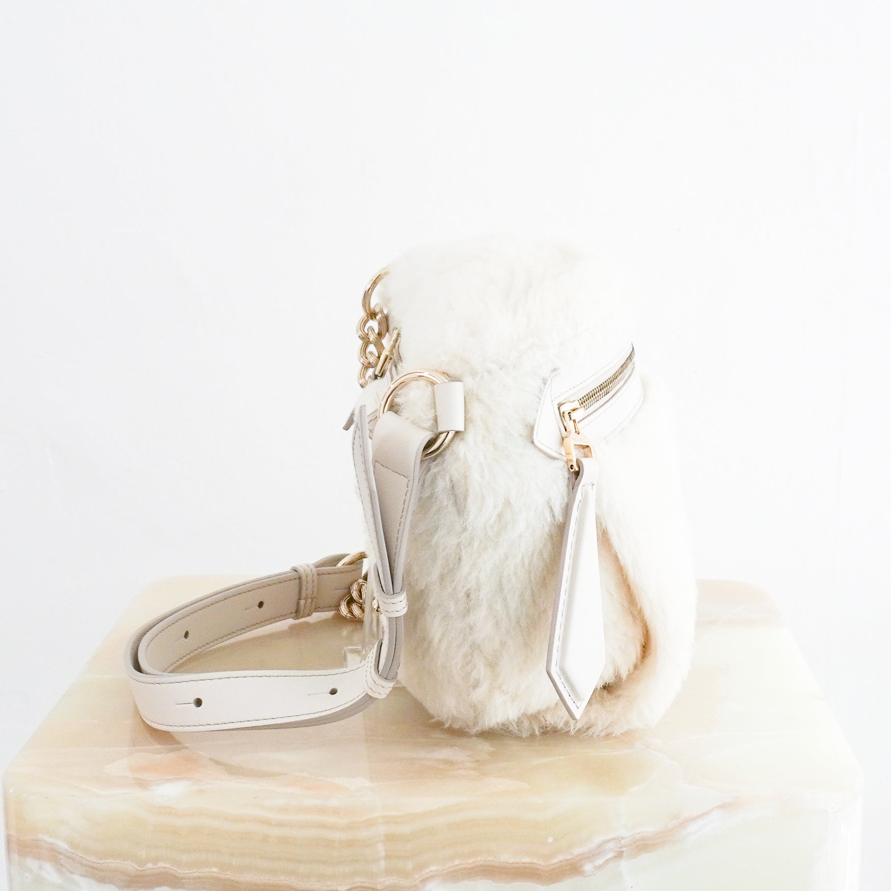 Side view photo of a MaxMara White Camelux Teddy Fur Shoulder Bag, featuring a plush textured exterior, gold-toned zipper hardware, and an attached leather strap