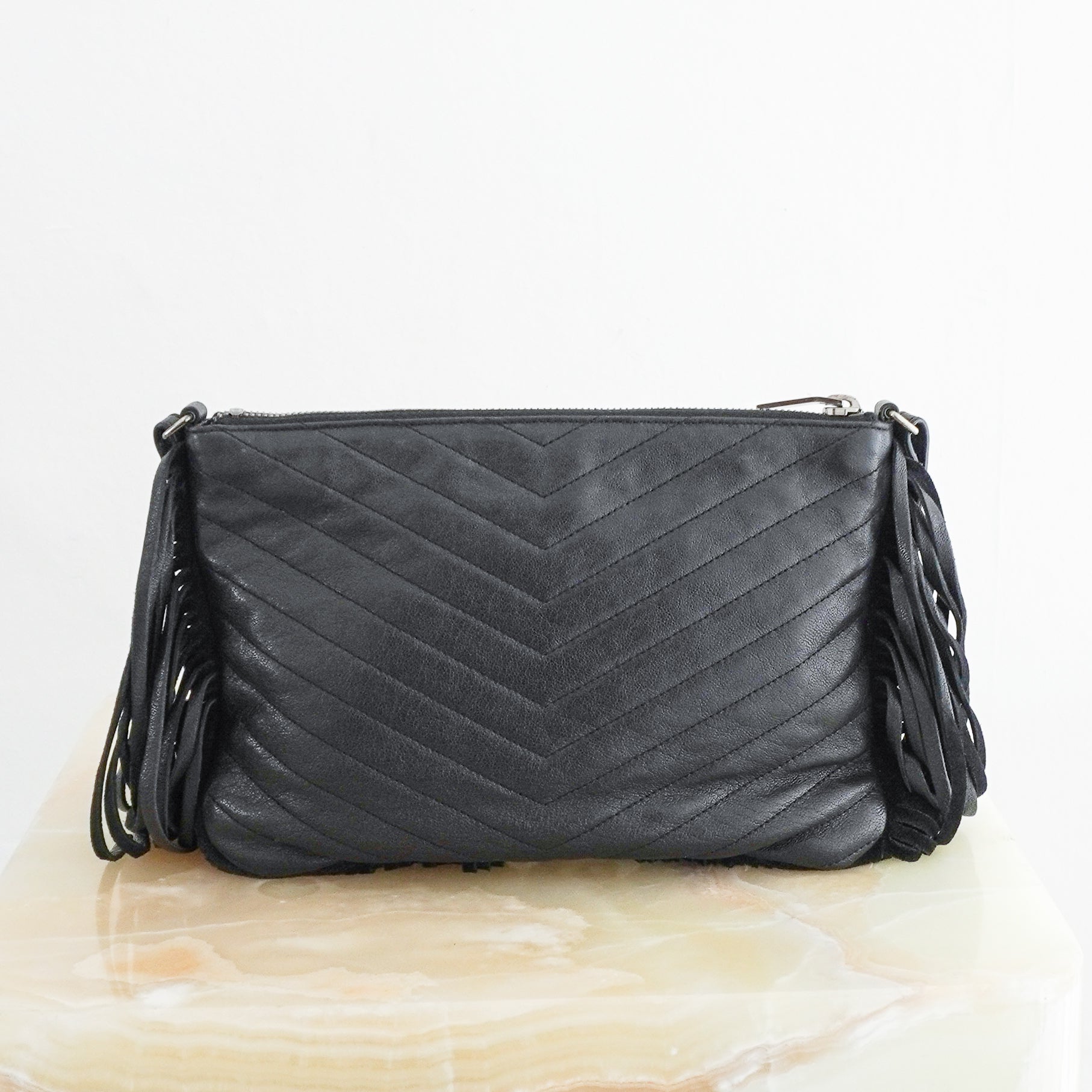 Back view photo of a Saint Laurent Monogram Fringe Leather Crossbody Bag in black, featuring chevron quilting, a silver-toned YSL logo, and long leather fringe detailing.