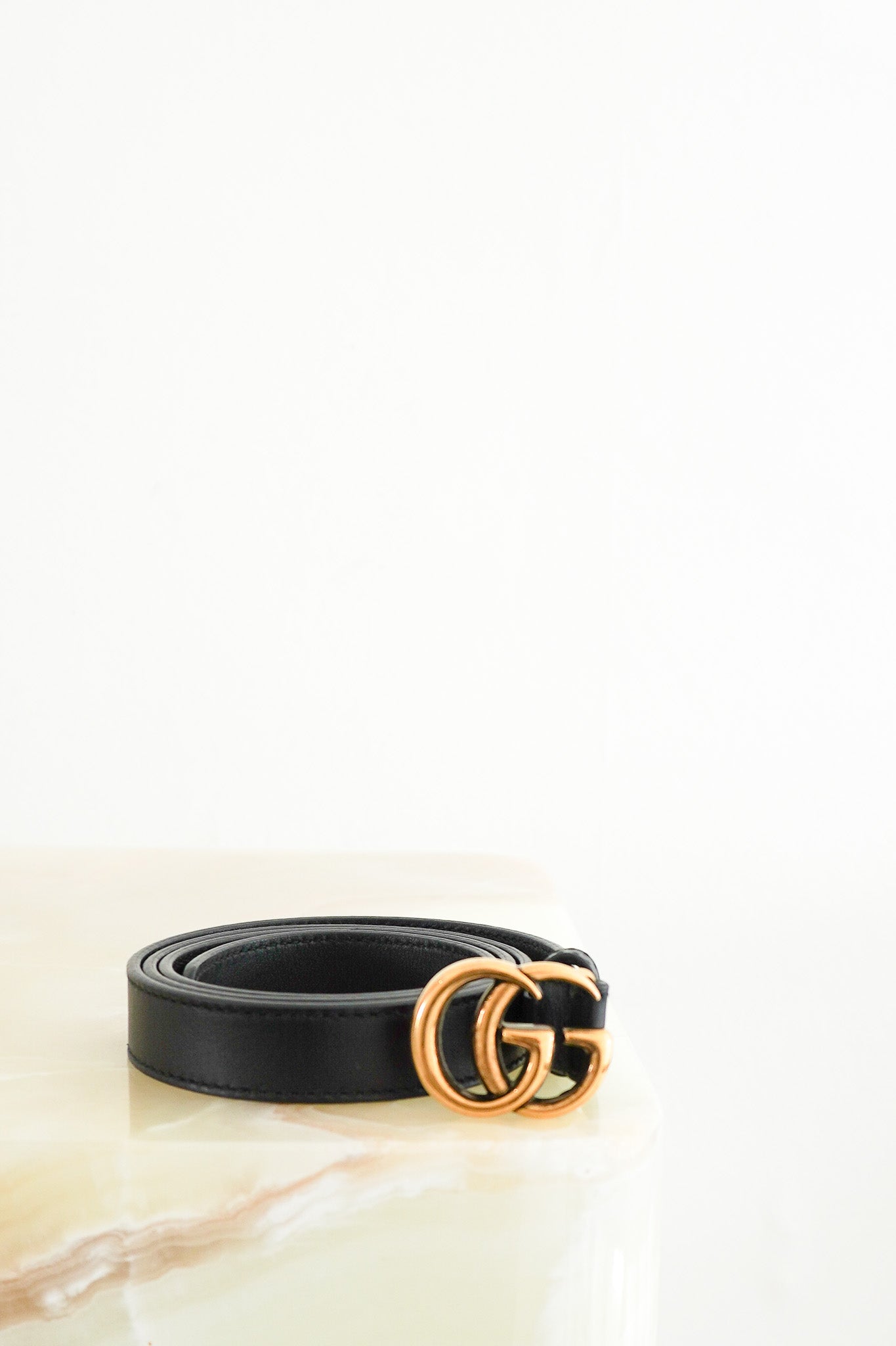 Front photo of a Gucci GG Black Skinny Leather Belt, featuring smooth black leather rolled into a coil with a prominent gold-tone double G monogram buckle.