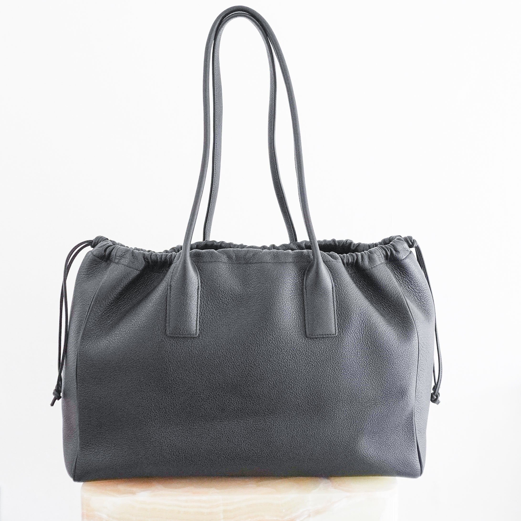 Back photo Celine Cuir Triomphe Cabas Drawstring Tote, crafted from luxurious black grained calfskin leather and featuring the house's iconic oversized embossed Triomphe logo to the front.
