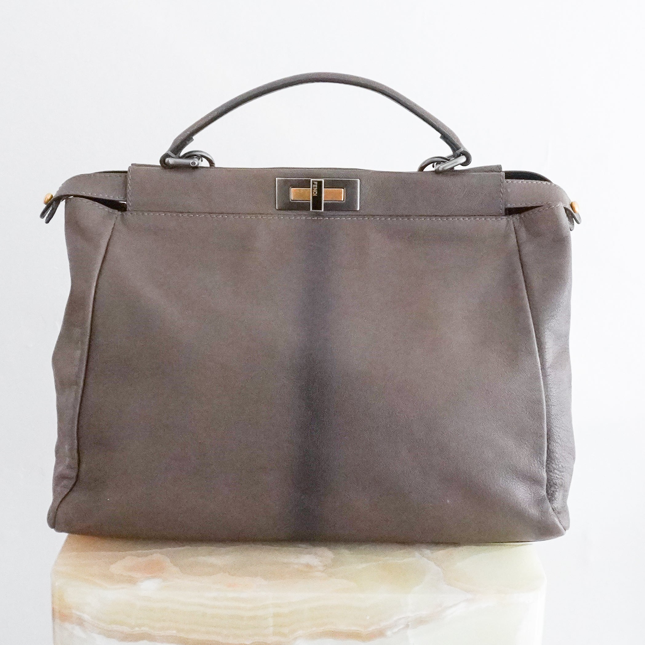 Back picture of a Fendi Peekaboo large satchel bag in taupe-grey leather with mixed silver and gold-tone hardware, a top handle and detachable shoulder strap, photographed on a cream marble pedestal.