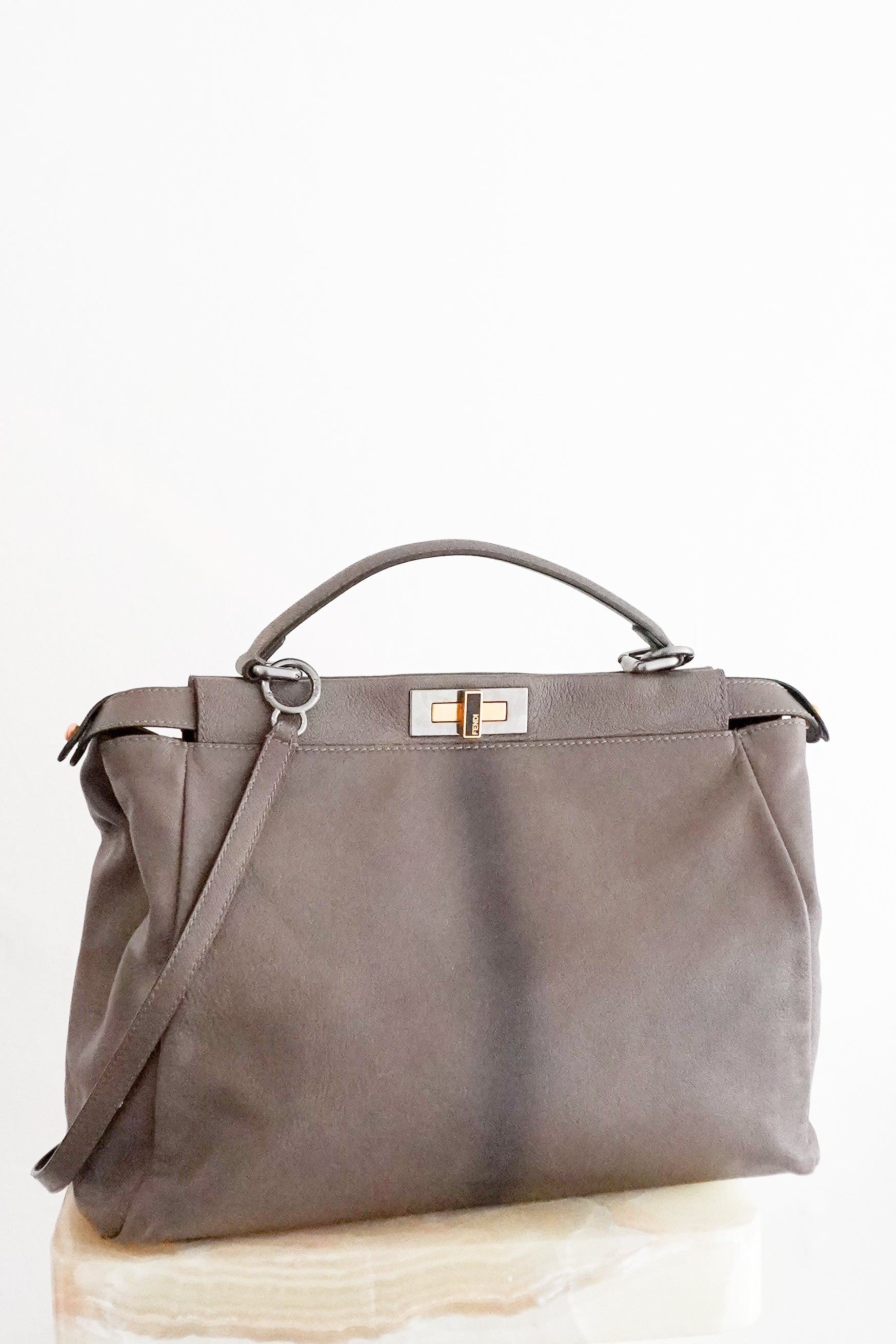 Front picture of a Fendi Peekaboo large satchel bag in taupe-grey leather with mixed silver and gold-tone hardware, a top handle and detachable shoulder strap, photographed on a cream marble pedestal.
