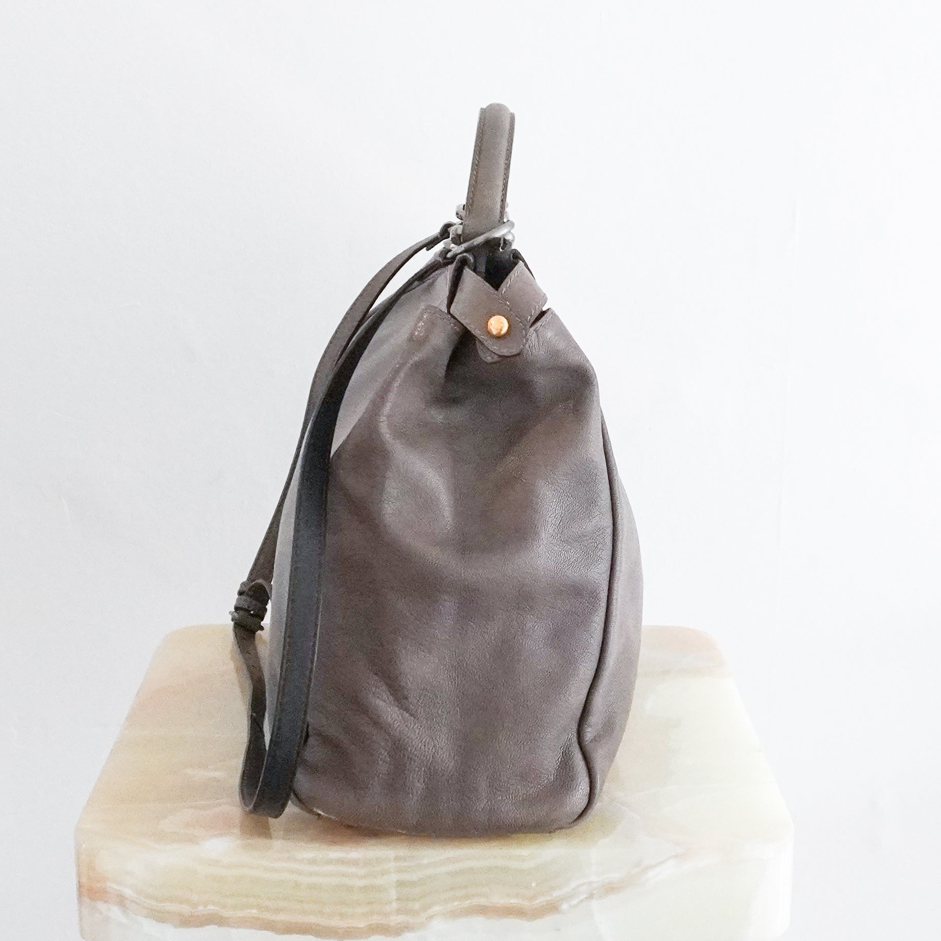 Side picture of a Fendi Peekaboo large satchel bag in taupe-grey leather with mixed silver and gold-tone hardware, a top handle and detachable shoulder strap, photographed on a cream marble pedestal.
