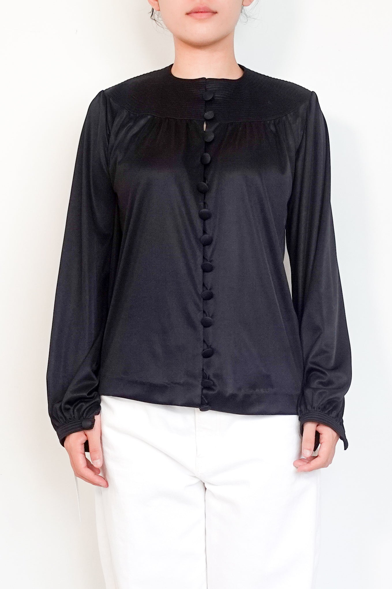 Person wearing a black button-up shirt and white pants against a plain background