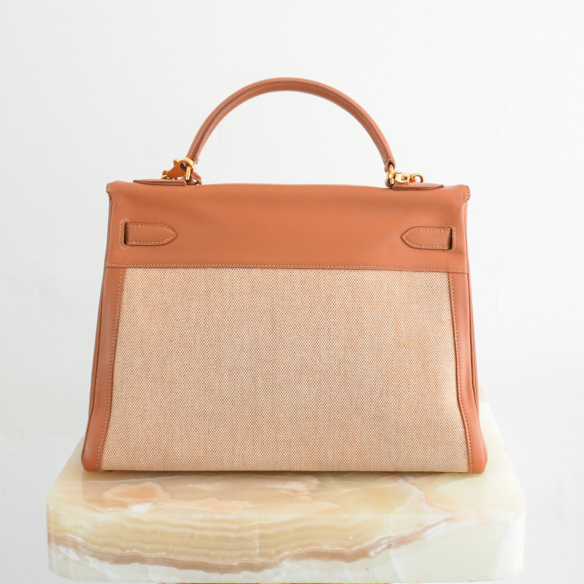 Back photo of an Hermès Kelly 32 handbag featuring tan Courchevel leather trim, a natural beige toile canvas body, gold-tone hardware, and a coordinating chevron patterned shoulder strap.