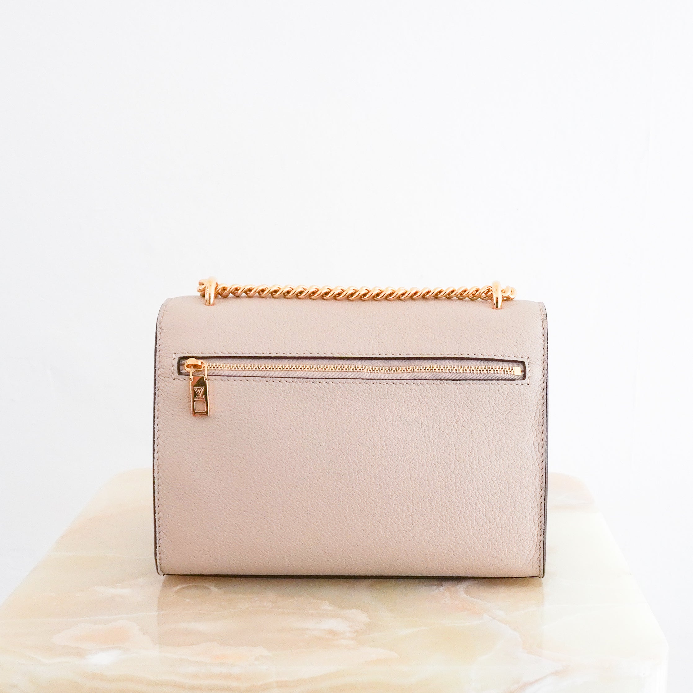 Louis Vuitton Lockme Chain Bag in greige grained calfskin leather featuring gold-tone hardware, the iconic LV turn-lock closure, exterior zipped pocket and leather-threaded chain strap