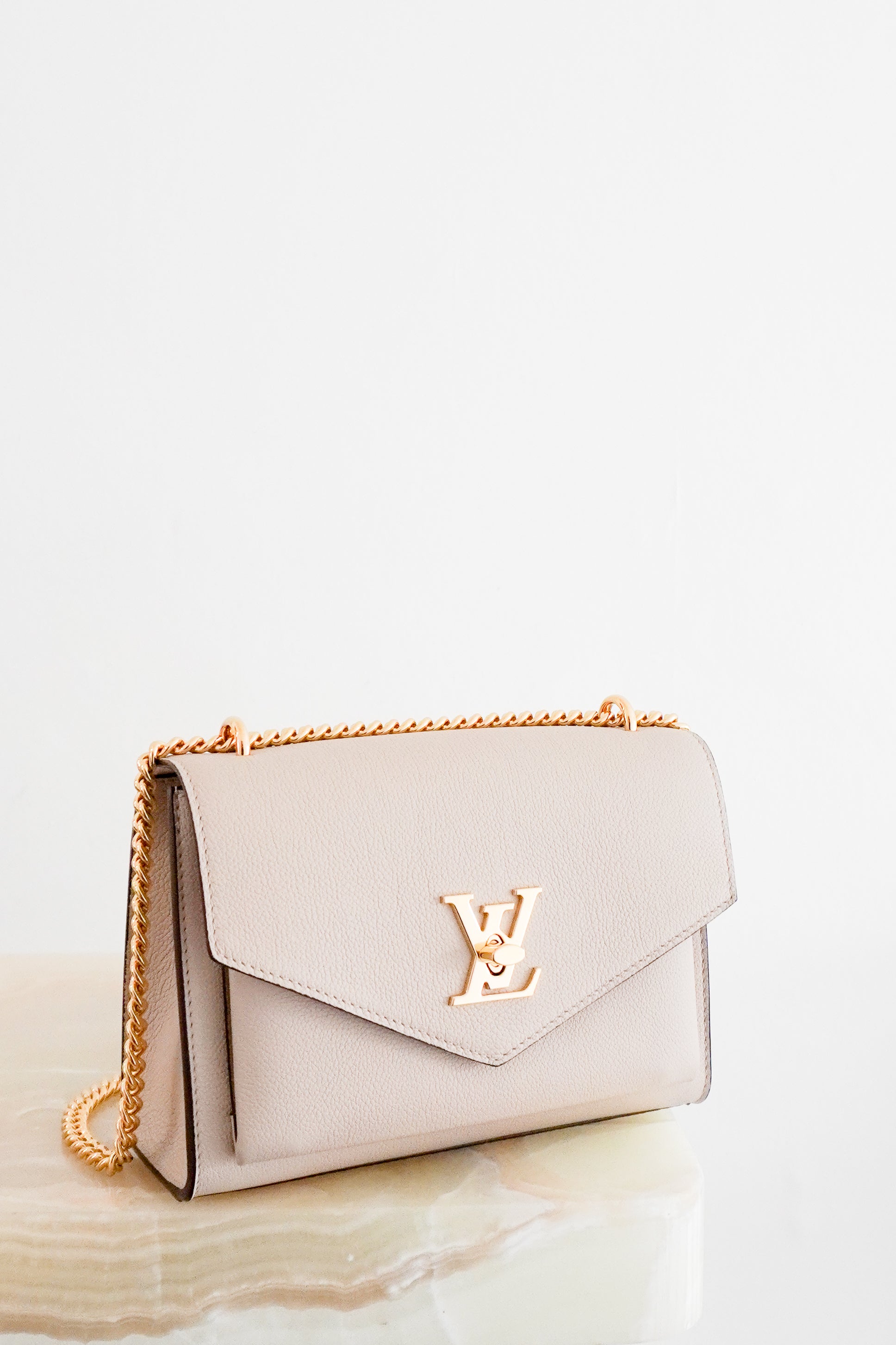 Louis Vuitton Lockme Chain Bag in greige grained calfskin leather featuring gold-tone hardware, the iconic LV turn-lock closure, exterior zipped pocket and leather-threaded chain strap