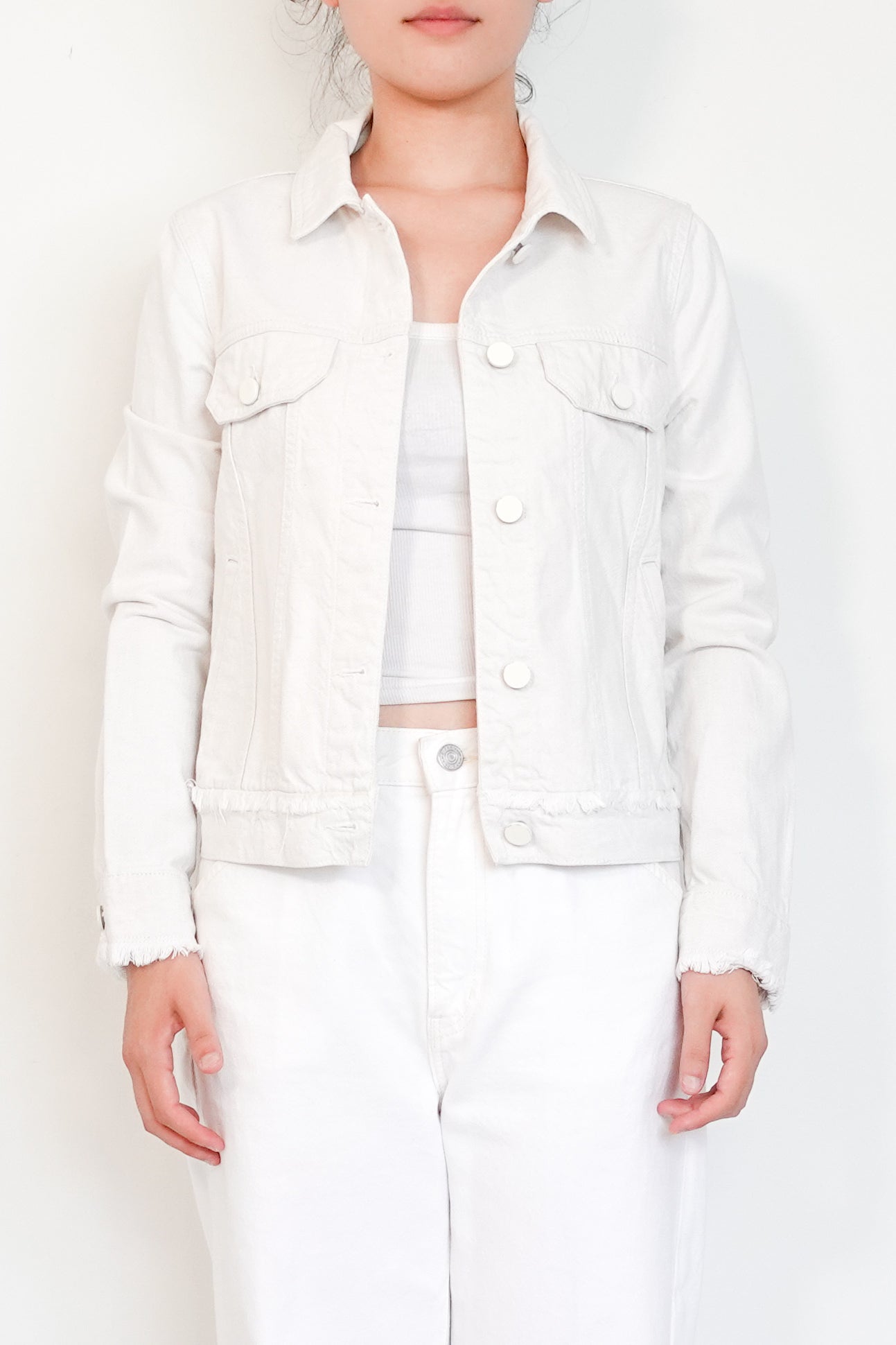 Person wearing a white denim jacket over a white shirt and pants on a plain background
