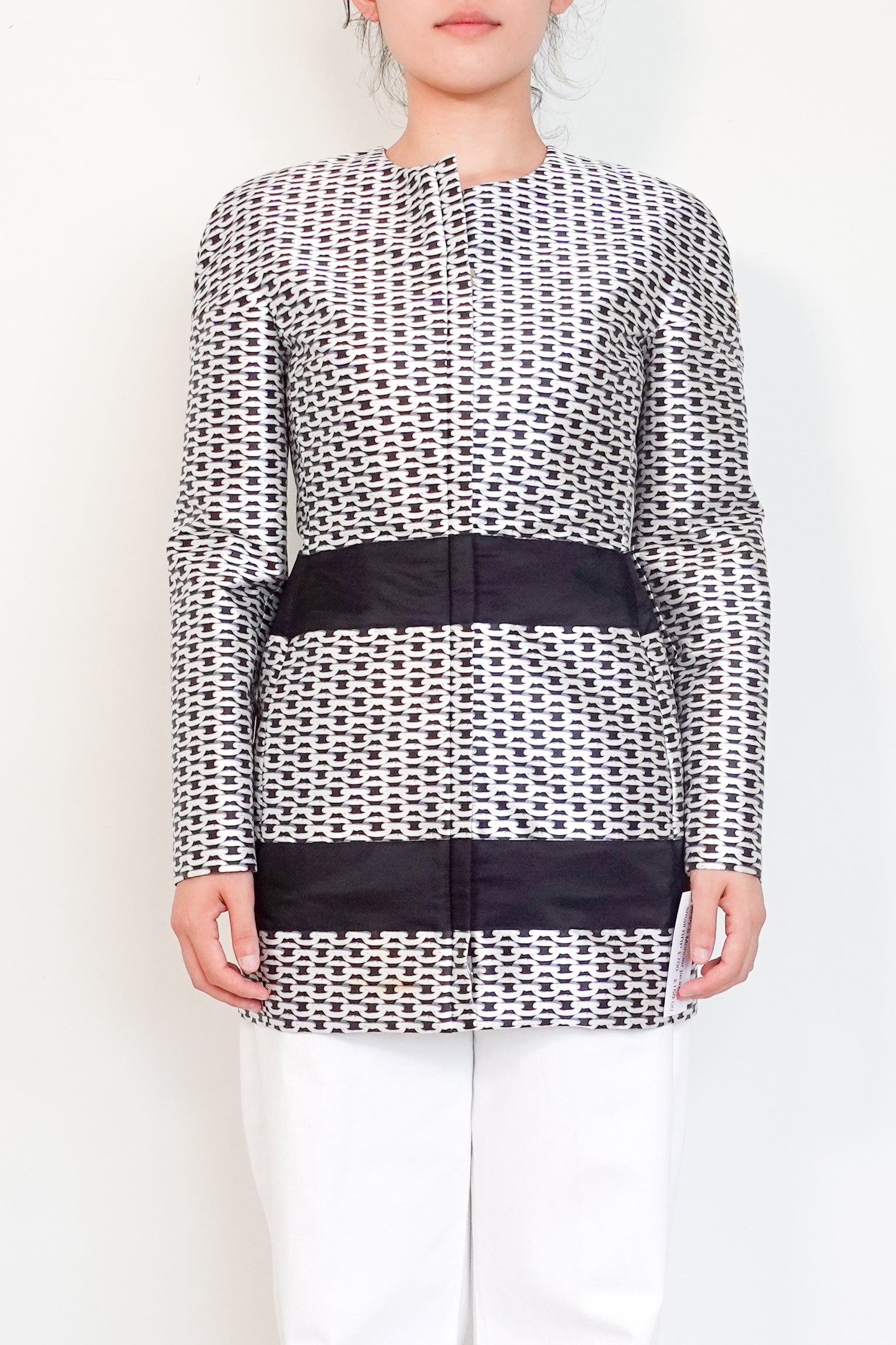 Person wearing a black and white patterned top with a wide belt on a plain background