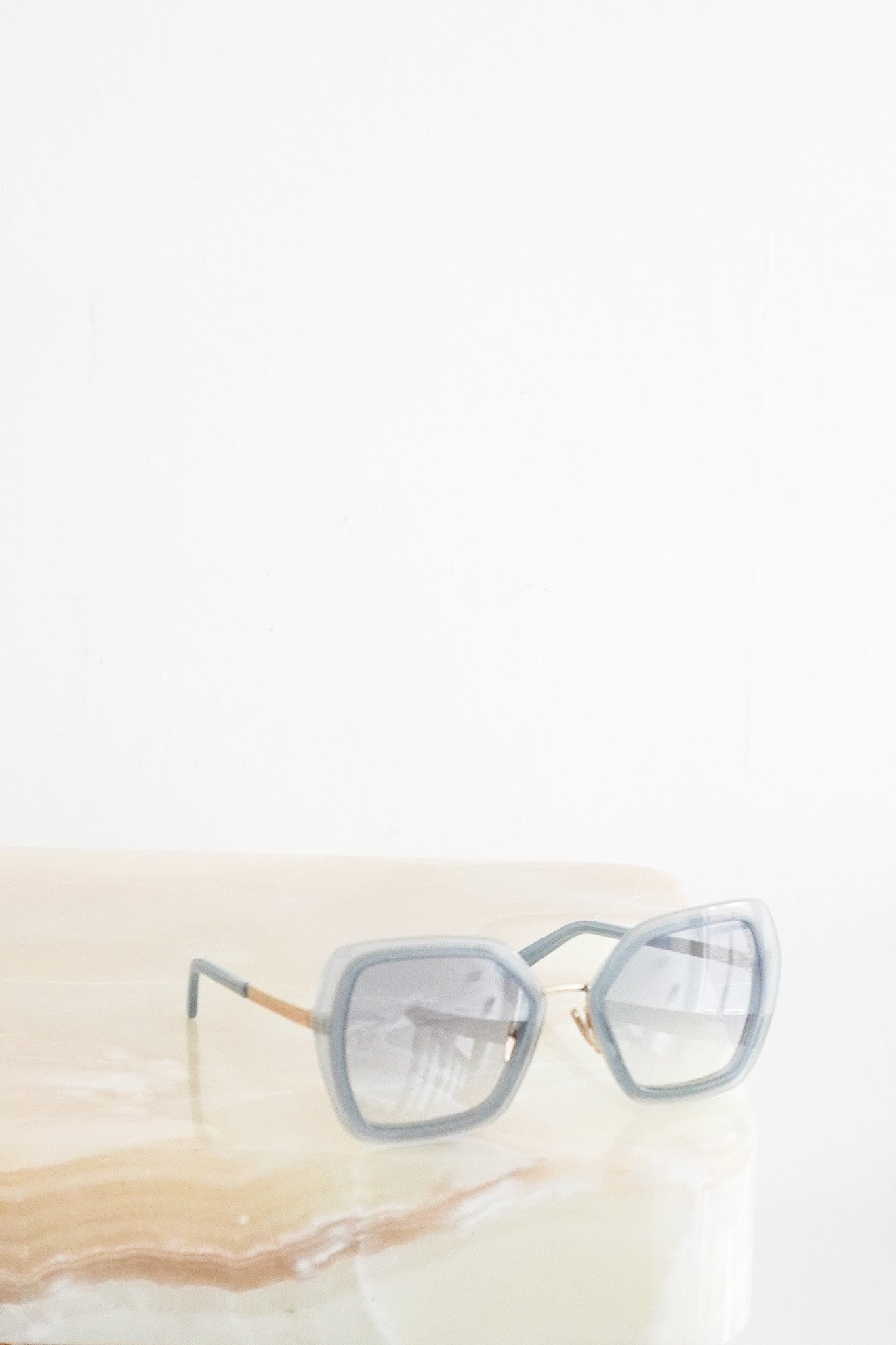 Front perspective of Prada light blue acetate sunglasses with pale blue tinted lenses on a white display.
