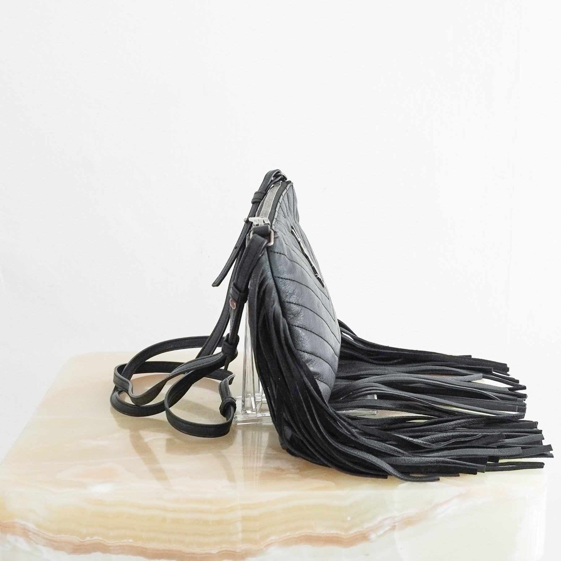 Side view photo of a Saint Laurent Monogram Fringe Leather Crossbody Bag in black, featuring chevron quilting, a silver-toned YSL logo, and long leather fringe detailing.