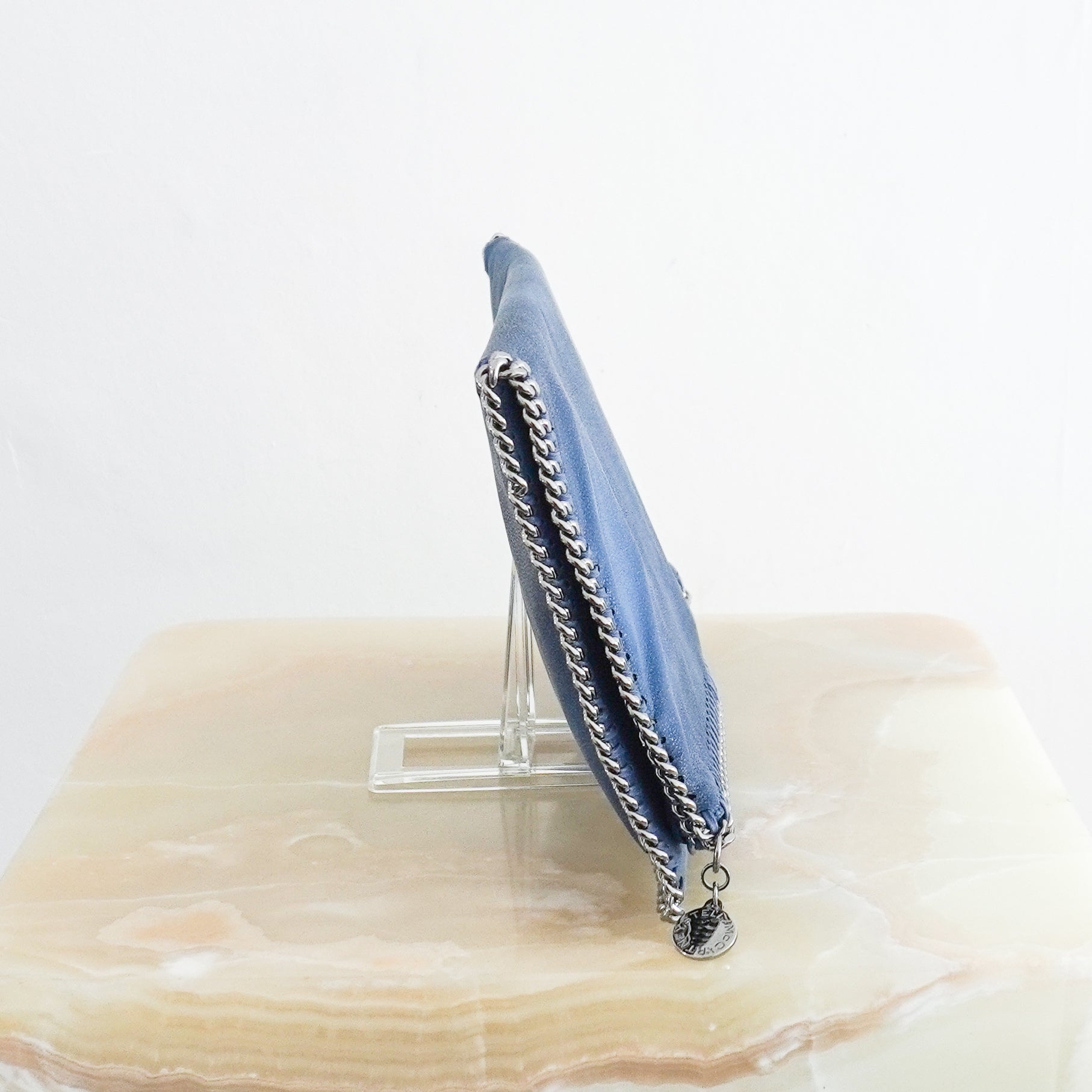 Side photo of Stella McCartney Blue Falabella Clutch Bag in faux leather featuring the signature silver chain trim and whipstitch detailing.